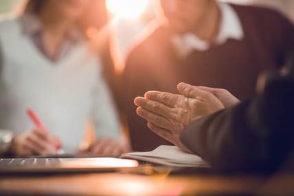 A meeting with an agent. A couple is in the background as an agent gestures and speaks with them while they sign a contract.